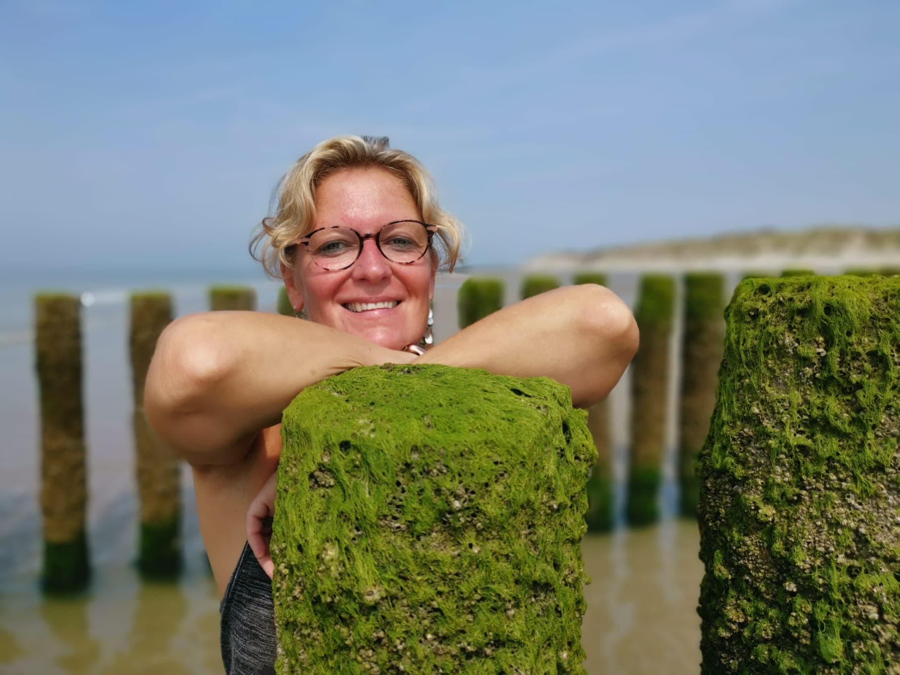 Rien Sanders glimlachend bij de palen aan het strand